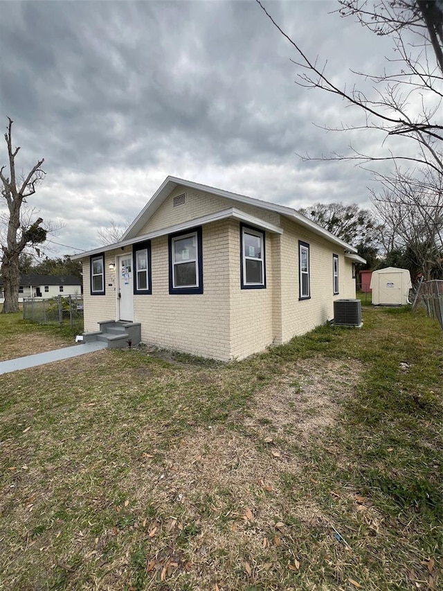 view of front facade with cooling unit, a storage shed, and a front lawn