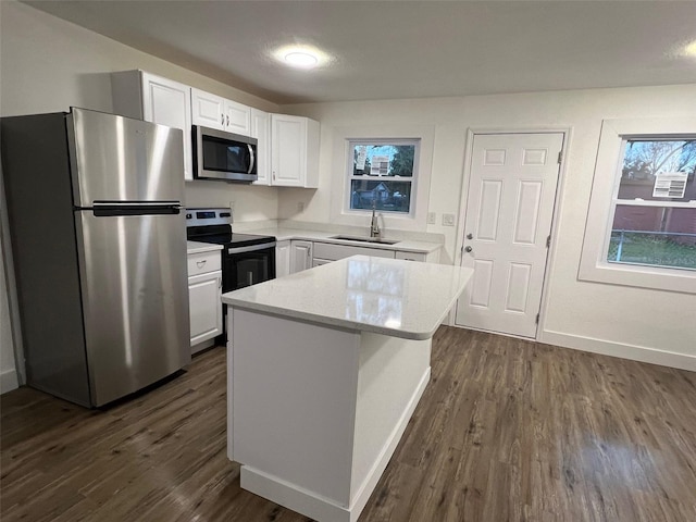 kitchen with appliances with stainless steel finishes, dark wood-type flooring, sink, white cabinets, and a kitchen island