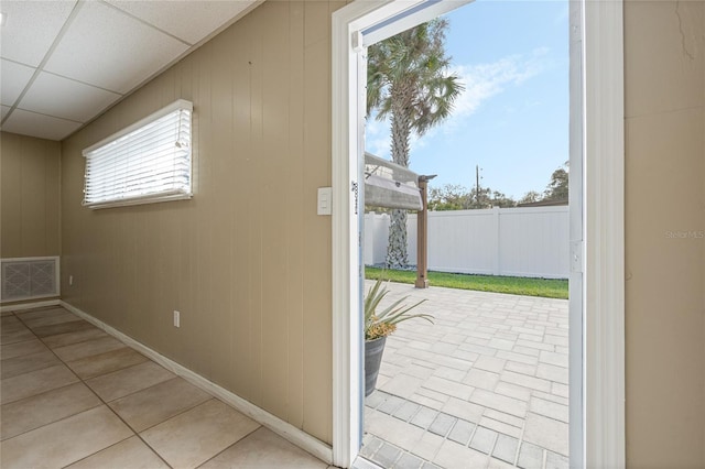 doorway with light tile patterned floors, plenty of natural light, and a drop ceiling