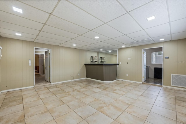 interior space with a paneled ceiling, wooden walls, and light tile patterned floors