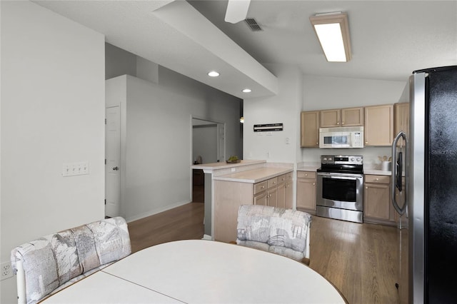 kitchen featuring dark hardwood / wood-style floors, kitchen peninsula, lofted ceiling, light brown cabinetry, and appliances with stainless steel finishes