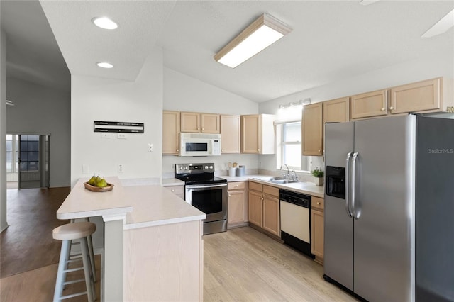 kitchen with a kitchen breakfast bar, sink, vaulted ceiling, appliances with stainless steel finishes, and kitchen peninsula