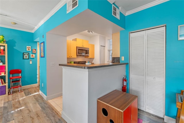 kitchen featuring kitchen peninsula, light brown cabinetry, light wood-type flooring, and ornamental molding