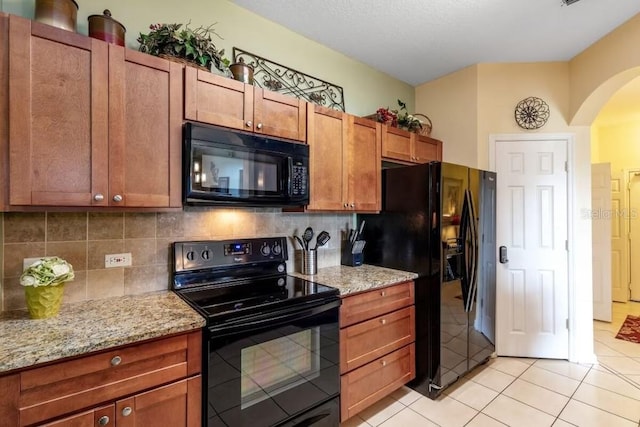 kitchen with light tile patterned flooring, tasteful backsplash, light stone countertops, and black appliances