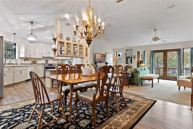 dining space with ceiling fan with notable chandelier, vaulted ceiling, sink, and light hardwood / wood-style flooring