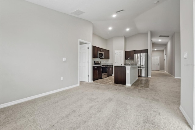 kitchen with dark brown cabinetry, stainless steel appliances, light colored carpet, a breakfast bar area, and a kitchen island with sink