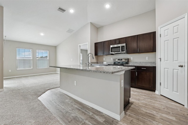 kitchen featuring light carpet, a center island with sink, sink, appliances with stainless steel finishes, and dark brown cabinets