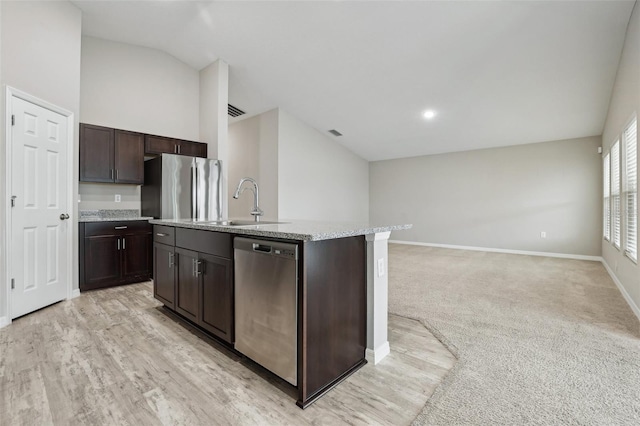 kitchen featuring a center island with sink, dark brown cabinets, light carpet, and appliances with stainless steel finishes