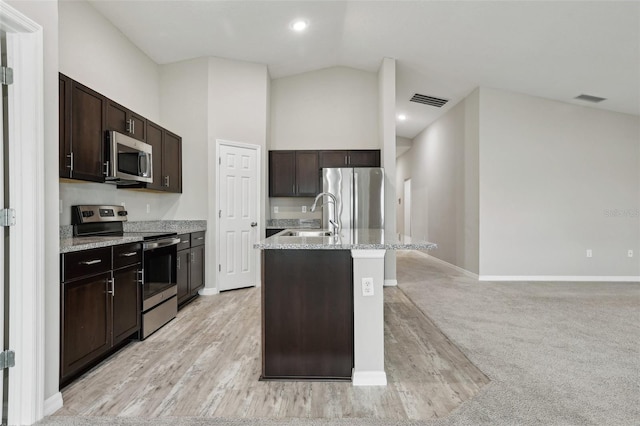 kitchen featuring dark brown cabinetry, sink, light colored carpet, a center island with sink, and appliances with stainless steel finishes