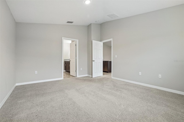 unfurnished bedroom with ensuite bathroom, light carpet, and vaulted ceiling