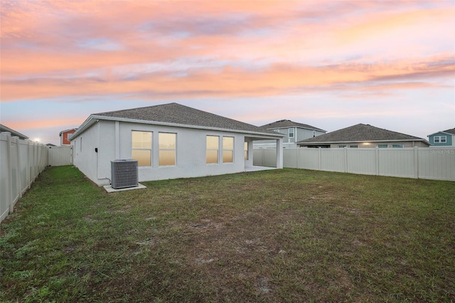 back house at dusk with cooling unit and a yard