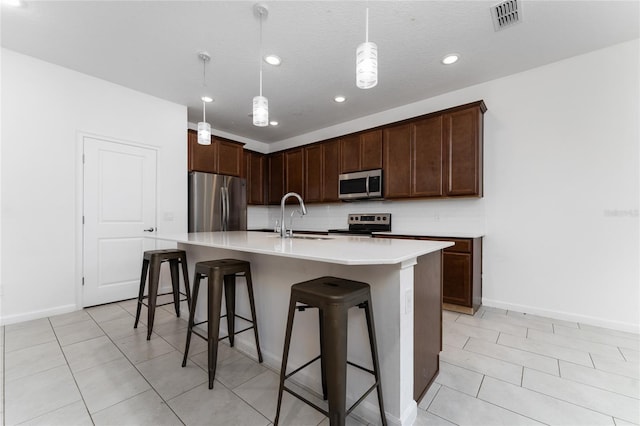 kitchen featuring decorative light fixtures, an island with sink, sink, a kitchen bar, and stainless steel appliances