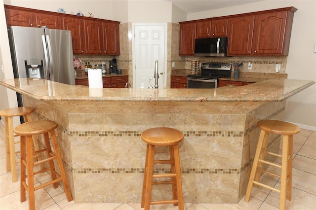 kitchen featuring kitchen peninsula, decorative backsplash, a breakfast bar, and stainless steel appliances