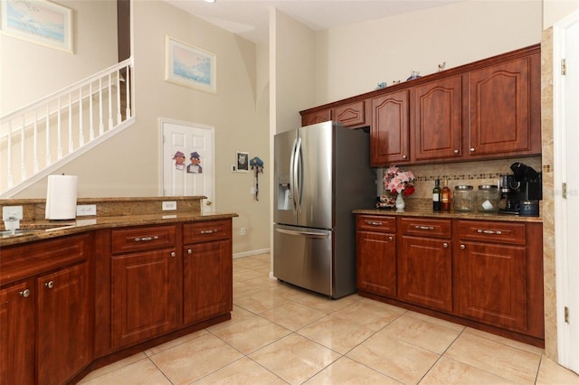 kitchen featuring stainless steel refrigerator with ice dispenser, backsplash, light tile patterned floors, and dark stone counters