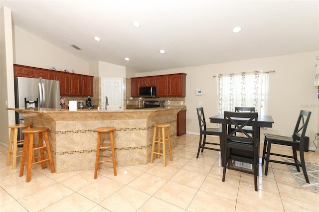 kitchen with a kitchen bar, appliances with stainless steel finishes, decorative backsplash, and lofted ceiling