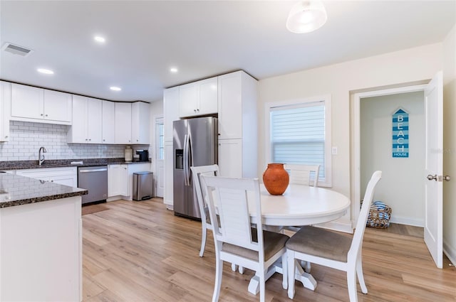 kitchen featuring appliances with stainless steel finishes, sink, white cabinets, decorative backsplash, and light hardwood / wood-style floors