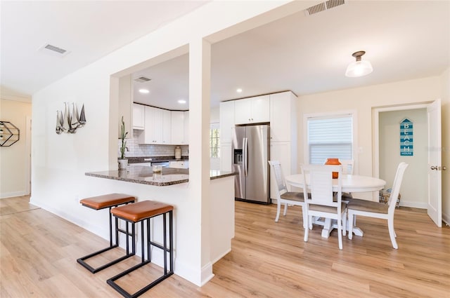 kitchen featuring stainless steel fridge with ice dispenser, kitchen peninsula, white cabinets, dark stone counters, and backsplash