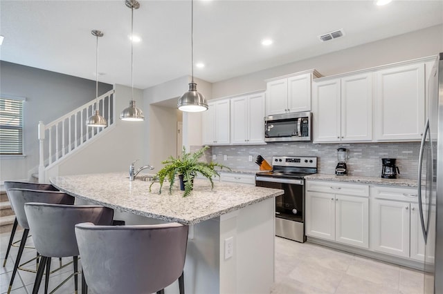 kitchen with white cabinetry, hanging light fixtures, a kitchen bar, a kitchen island with sink, and appliances with stainless steel finishes