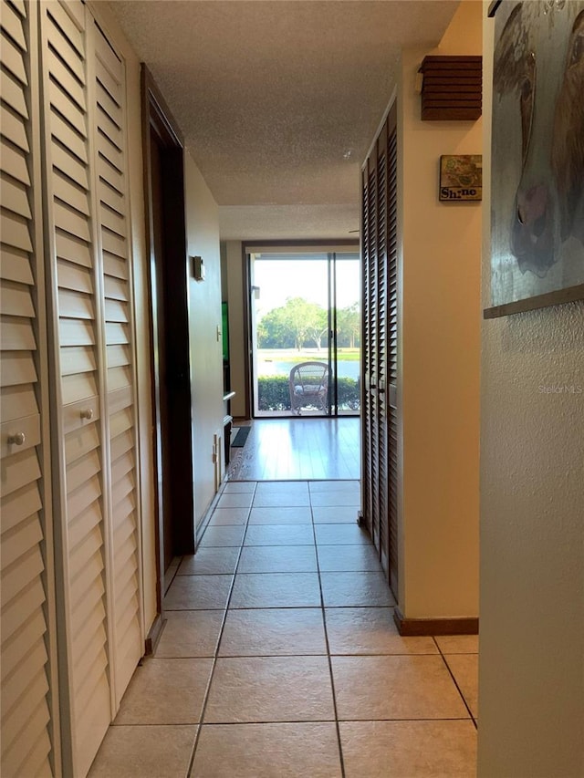 hallway featuring light tile patterned floors, baseboards, and a textured ceiling