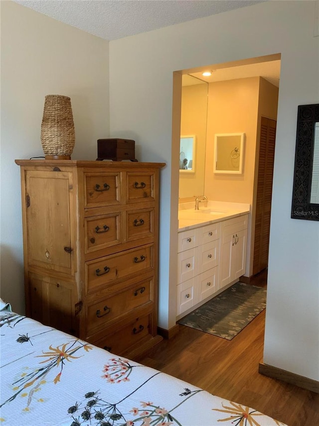 bedroom with a textured ceiling, a sink, baseboards, dark wood-style floors, and ensuite bath