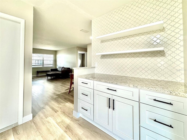 kitchen featuring tasteful backsplash, light stone counters, white cabinets, and light wood-type flooring