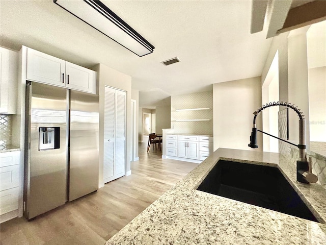 kitchen with light stone countertops, stainless steel fridge, light wood-type flooring, sink, and white cabinets