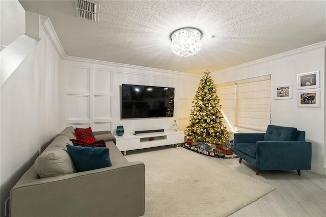 living room with a textured ceiling, light hardwood / wood-style flooring, ornamental molding, and a notable chandelier