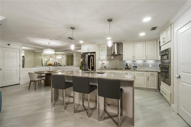 kitchen with white cabinets, wall chimney range hood, stainless steel appliances, and hanging light fixtures