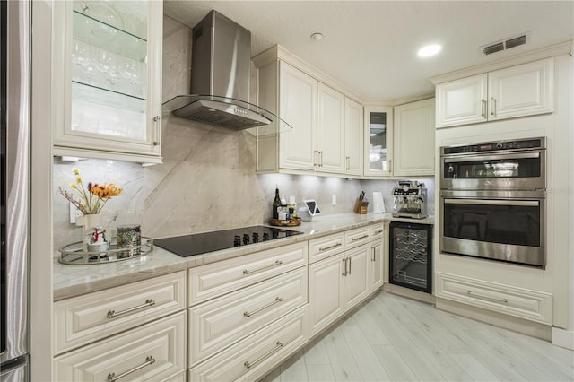 kitchen featuring wall chimney exhaust hood, stainless steel double oven, beverage cooler, light stone counters, and black electric cooktop