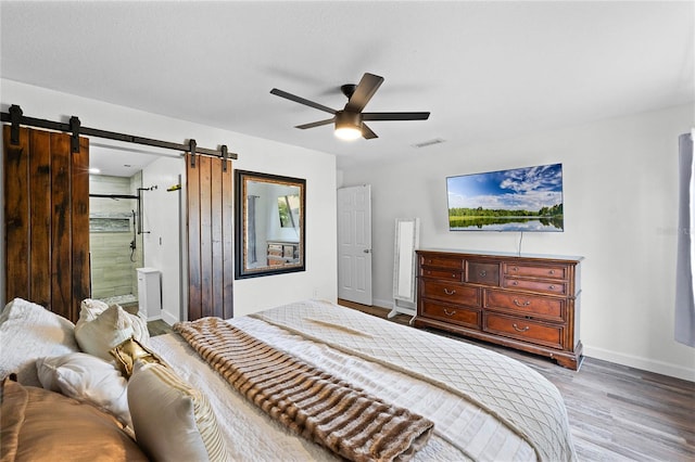 bedroom featuring hardwood / wood-style floors, a barn door, ensuite bath, and ceiling fan