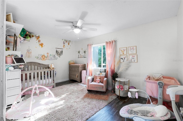 bedroom with a crib, dark hardwood / wood-style floors, and ceiling fan