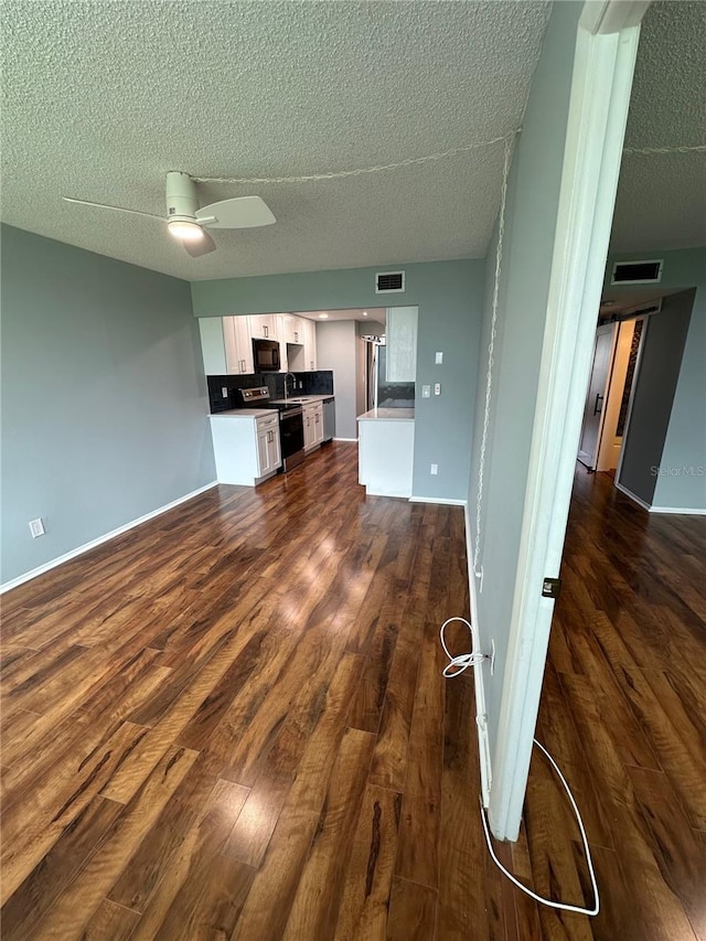 unfurnished living room featuring a textured ceiling, ceiling fan, dark hardwood / wood-style flooring, and sink