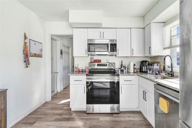 kitchen with light stone countertops, white cabinetry, stainless steel appliances, and light hardwood / wood-style flooring