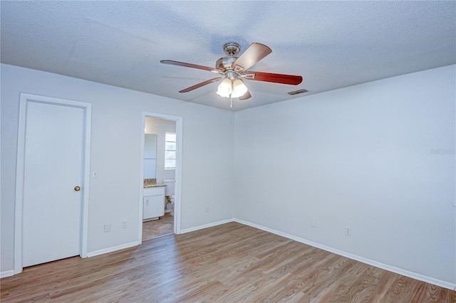 unfurnished bedroom with ceiling fan, a textured ceiling, ensuite bathroom, and light wood-type flooring