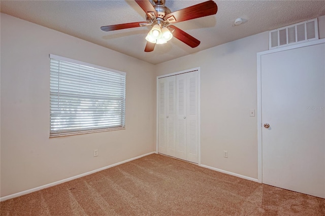 unfurnished bedroom featuring a closet, ceiling fan, light colored carpet, and a textured ceiling