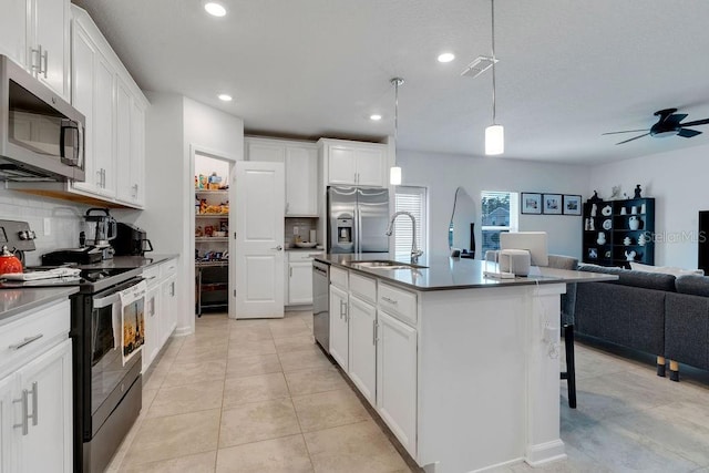 kitchen with stainless steel appliances, a kitchen island with sink, sink, white cabinets, and hanging light fixtures