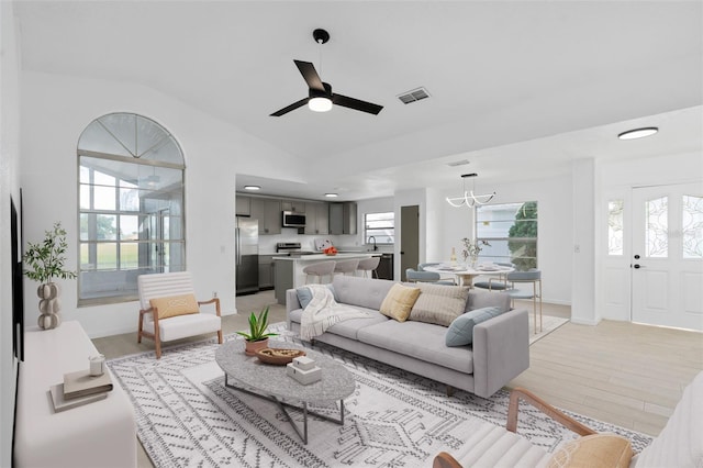 living room featuring ceiling fan with notable chandelier, light wood-type flooring, lofted ceiling, and sink