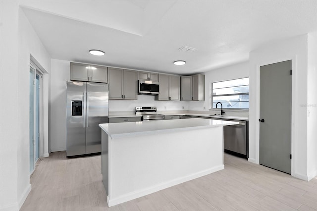 kitchen featuring gray cabinetry, sink, light hardwood / wood-style flooring, appliances with stainless steel finishes, and a kitchen island