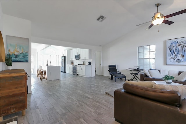 living room featuring ceiling fan, light wood-type flooring, sink, and vaulted ceiling