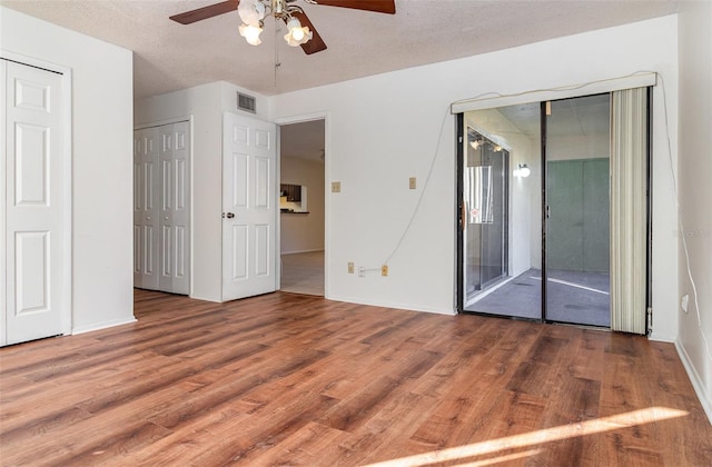 unfurnished bedroom with access to exterior, a textured ceiling, two closets, ceiling fan, and hardwood / wood-style flooring