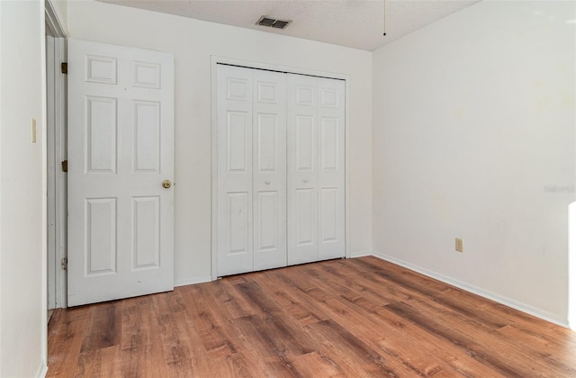 unfurnished bedroom with wood-type flooring, a textured ceiling, and a closet