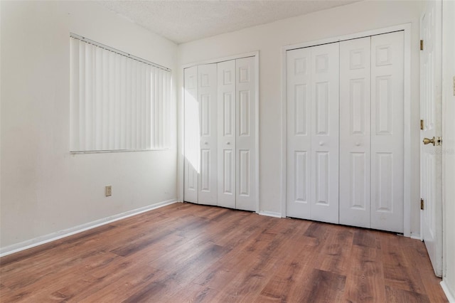 unfurnished bedroom with wood-type flooring, a textured ceiling, and multiple closets
