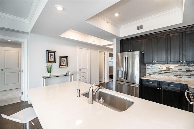 kitchen featuring decorative backsplash, sink, stainless steel fridge, a raised ceiling, and a breakfast bar area