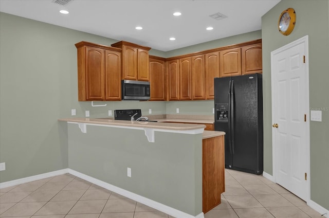 kitchen featuring a kitchen bar, black fridge, kitchen peninsula, and light tile patterned floors