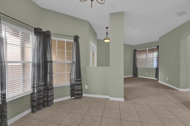 tiled spare room featuring a wealth of natural light and a notable chandelier