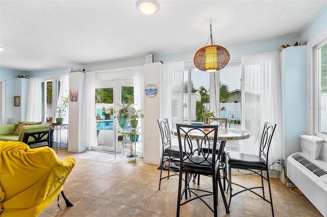 dining area featuring light tile patterned floors, radiator heating unit, a textured ceiling, and a healthy amount of sunlight