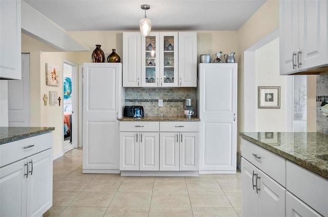 kitchen featuring white cabinetry, hanging light fixtures, tasteful backsplash, dark stone countertops, and light tile patterned floors