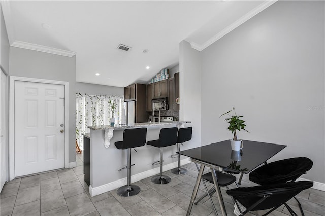 kitchen featuring visible vents, dark brown cabinetry, a peninsula, a breakfast bar area, and black microwave