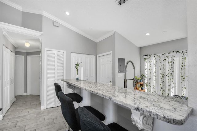 kitchen featuring visible vents, a breakfast bar, ornamental molding, light stone counters, and a peninsula