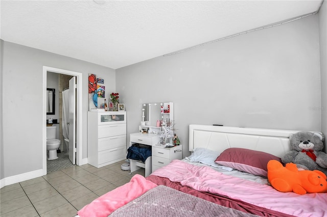 bedroom featuring light tile patterned floors, baseboards, ensuite bathroom, and a textured ceiling